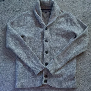 Grå kofta från Tommy Hilfiger - Säljer en stilren grå kofta från Tommy Hilfiger med knappar framtill. Den har en bekväm passform och är perfekt för kyligare dagar. Koftan är långärmad och har ribbade muddar vid ärmslut och nederkant. Nypris runt 1349 mitt pris 699. Koftan är nästan helt ny och är ej nopprig. Kan tänka mig gå ner vid pris vid snabb affär. Priset är ej hugget i sten så bara lägga prisförslag. Skick 9/10🤩😮‍💨