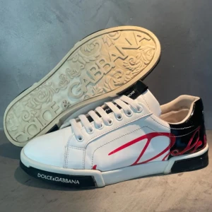 Vita sneakers från Dolce & Gabbana - Stilrena vita sneakers från Dolce & Gabbana med svart och röd detaljering. Skorna har sprickor har kvitto och är köpta från sneakerstv. har du några frågor ställ de!