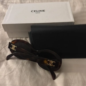 Bruna solglasögon från Celine - Säljer ett par snygga bruna solglasögon från Celine i mycket bra skick. De har en klassisk rund form med ett elegant guldmärke på sidorna. Perfekta för att ge din outfit en lyxig touch. Kommer med originalfodral och box. Priset går alltid att diskutera! Dessa är äkta! 