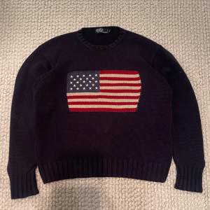 Säljer en snygg mörkblå tröja från Polo Ralph Lauren i storlek L. Den är gjord av 100% bomull och har en amerikansk flagga på framsidan. Perfekt för höst och vinter. Skriv om du har frågor!