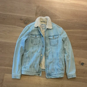 Ljusblå jeansjacka med foder - Säljer en snygg ljusblå jeansjacka med mysigt foder. Perfekt för höst och vår! Jackan har två bröstfickor med knappar och två sidofickor. Den är långärmad och har en klassisk krage. Passar både till vardags och lite mer uppklädda tillfällen.