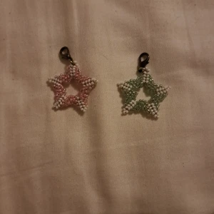 Stjärnformade pärlhängen i rosa och grönt - Två söta stjärnformade hängen gjorda av små pärlor, gjort dom själv. Ett hänge är i rosa och vitt, och det andra i grönt och vitt. Perfekta som dekorationer eller att fästa på väskor och nyckelringar. De har en liten klämma för enkel fastsättning. Supergulliga och unika!