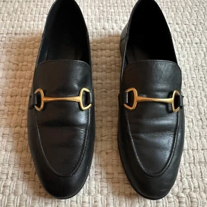 Svarta loafers från Massimo Dutti - Snygga svarta loafers i skinn från Massimo Dutti, säljes då de inte kommer till användning. De har en elegant guldfärgad detalj på ovansidan som ger en lyxig touch. Perfekta för både vardag och festliga tillfällen. Skorna är i mycket bra skick. Passar perfekt till både jeans och kostym!