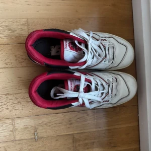 New Balance 550 sneakers - Säljer ett par New Balance 550 sneakers i vitt och rött. De har en klassisk design med snörning och är i bra skick. Perfekta för både vardag och träning. Storlek och passform är normal.
