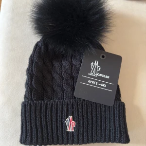 mössa från Moncler - Säljer en snygg svart stickad mössa från Moncler med en fluffig pälsboll på toppen. Den är äkta , kvitto finns 
