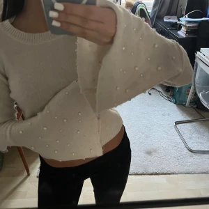 Vit stickad tröja med pärldetaljer - Säljer en superfin vit stickad tröja med pärlor på ärmarna. Den är croppad och har en öppen rygg med knytband. Perfekt för både höst och vår! Tröjan har långa ärmar och är i mycket bra skick. Passar perfekt till både jeans och kjol.