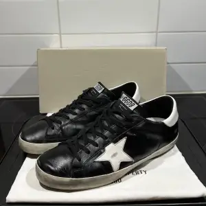 Säljer ett par snygga svarta sneakers från Golden Goose. Dom är i nyskick endast använda fåtal gånger, original lådan och skopåsen medföljer vid köp. Dom är givetvis äkta och köpte från en verifierad säljare på vestiare kvitto kan fixas!