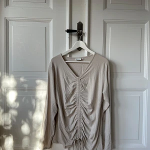 Beige långärmad topp med snörning - Säljer en superfin beige långärmad topp med snörning framtill. Perfekt för både vardag och fest! Den har en v-ringad design och är i ett mjukt och bekvämt material. Passar perfekt till jeans eller kjol.