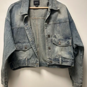 Jeansjacka från Boohoo - Säljer en snygg jeansjacka från Boohoo i storlek L. Den har en klassisk blå tvätt och är utrustad med knappar framtill och två bröstfickor med lock. Jackan är i bra skick och har inte används förutom en gång för att se om den passade.