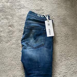 Säljer ett par snygga blå jeans från Dondup i nytt skick. De har en cool slitning och distressed look som ger en avslappnad stil. Perfekta för både vardag och fest! Tillverkade i Italien med hög kvalitet.  Detta är modellen George som är destroyed från fabrik vilket gör den sjukt populär, denna dondup byxa är enligt mig den snyggaste modellen man kan ha, sprillans nya med tagg kvar, köpta av en special leverantör dock en liten defekt i skrevet ( inget man tänker på!)  MVH// 101 CLOSET, göteborg🙌🏼