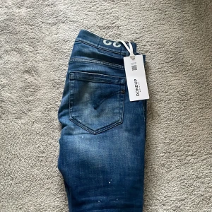 Dondup George NYA - Säljer ett par snygga blå jeans från Dondup i nytt skick. De har en cool slitning och distressed look som ger en avslappnad stil. Perfekta för både vardag och fest! Tillverkade i Italien med hög kvalitet.  Detta är modellen George som är destroyed från fabrik vilket gör den sjukt populär, denna dondup byxa är enligt mig den snyggaste modellen man kan ha, sprillans nya med tagg kvar, köpta av en special leverantör dock en liten defekt i skrevet ( inget man tänker på!)  MVH// 101 CLOSET, göteborg🙌🏼