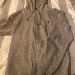 Ralph lauren zip - Säljer en grå hoodie ifrån Us polo assn i bra skick med dragkedja och justerbar huva. Perfekt för höst och vinter, supermysig och enkel att matcha med allt. Det är inte en Ralp lauren vet inte varför det blir så säljer även en i svart DM för frågor💯👍🙌