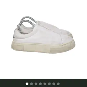 Säljer ett par vita sneakers i bra skick med en cool lila detalj på hälen. De har en klassisk design med en något smutsig sula som ger dem en avslappnad look. Perfekta för vardagsbruk och passar till det mesta i garderoben.