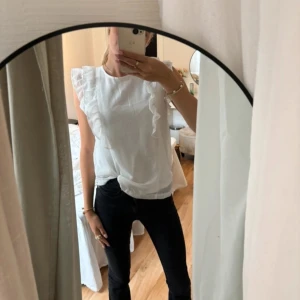 Vit blus med volangdetaljer - Lånade bilder! Köpt på vinted i år. Säljer en superfin vit blus med volangdetaljer. Den har en söt knytning i ryggen och är perfekt för både vardag och fest. Blusen är ärmlös och har en luftig passform. Passar perfekt till både jeans och kjol!