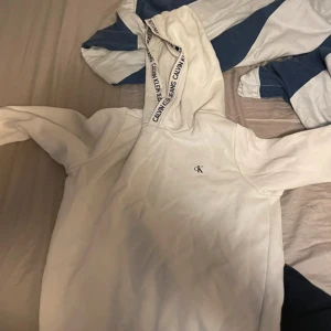 Vit hoodie från Calvin Klein - Säljer en snygg vit hoodie från Calvin Klein. Den har en liten CK-logga på bröstet och text på huvan. Supermjuk och bekväm!