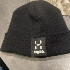 Svart mössa från Haglöfs - Snygg och stilren svart mössa från Haglöfs i stickat material. Perfekt för kalla dagar med sin enkla design och varma känsla. Märkesloggan är tydligt broderad framtill. Passar både till vardags och utomhusaktiviteter.