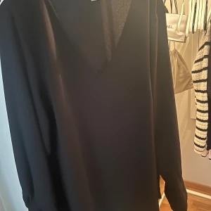 Svart skjorta med nitar - Säljer en elegant svart skjorta i storlek L. Den har långa ärmar och är dekorerad med små nitar längs ärmsluten och halsringningen. Perfekt för en kväll ute eller en festlig tillställning. Skjortan är i mycket bra skick och ger en stilren look.