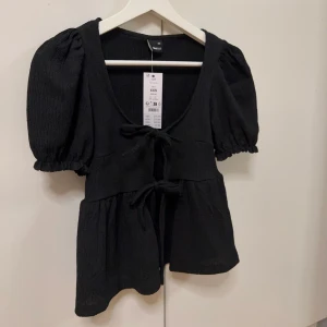 Svart blus - Säljer en supersnygg svart blus från Gina tricot i storlek XXS. Den har korta puffärmar och en söt knytning framtill. Perfekt för både vardag och fest! Säljes pga för liten🥰
