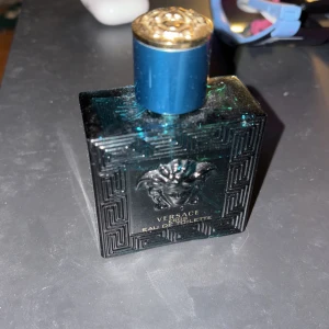 Versace Eros Eau de Toilette - Säljer en flaska Versace Eros Eau de Toilette. Flaskan är fyrkantig och mörkblå med ett snyggt mönster och Versaces ikoniska Medusa-logga på framsidan. Korken är också blå med en gyllene topp. Perfekt för den som vill ha en fräsch och maskulin doft. Passar både till vardags och fest!