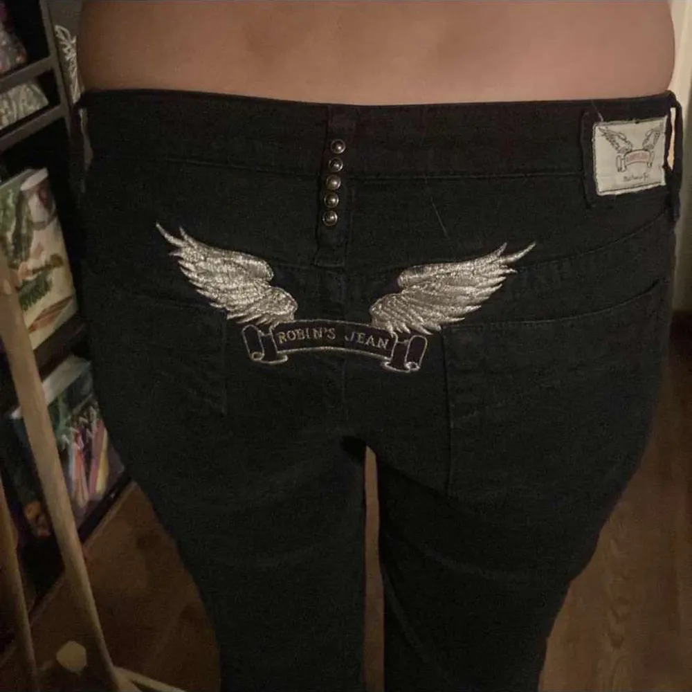 Snygga svarta jeans från Robin's Jean med coola broderade vingar på bakfickorna. De har en låg midja och en bootcut-stil som ger en retro vibe. Perfekta för både vardag och fest! 🖤midjemått tvärs över 39cm. Innerbenslängd 80cm.. Jeans & Byxor.