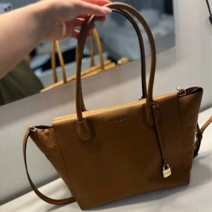 Brun handväska från Michael Kors - Säljer en snygg brun handväska från Michael Kors i mycket bra skick. Väskan är gjord av skinn och har en praktisk dragkedja upptill. Perfekt för både vardag och fest! 👜✨