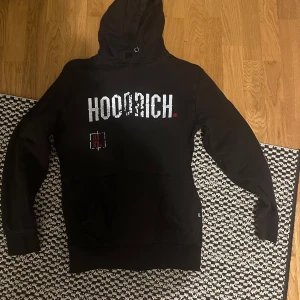 Svart hoodie från Hoodrich - Säljer en svart hoodie från Hoodrich i bra skick. Den har en stor logga på framsidan och en detaljerad design på baksidan. Perfekt för höst och vinter, med en skön passform och huva för extra värme. Passar både till vardags och chill.