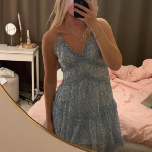 Blå blommig klänning - Säljer en superfin blå klänning med blommigt mönster. Den har smala axelband och volangdetaljer som ger en romantisk känsla. Perfekt för sommarens fester eller en mysig vårdag. Klänningen är i mycket bra skick och har en luftig passform.