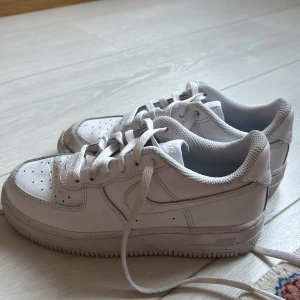 Vita Nike Air Force sneakers - Säljer ett par klassiska vita Nike Air Force sneakers i bra skick. De har en stilren design med snörning och är perfekta för vardagsbruk. Skorna är bekväma och passar till det mesta i garderoben. Perfekta för både vår och sommar! Skorna är i storlek 30 och är knappast använda. 