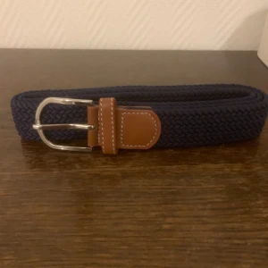 Blått flätat bälte med bruna detaljer - Säljer ett snyggt blått flätat bälte med bruna läderdetaljer och ett silverfärgat spänne. Perfekt för både vardag och fest! Bältet är i mycket bra skick och passar de flesta outfits. Ett måste i garderoben för den stilmedvetna.