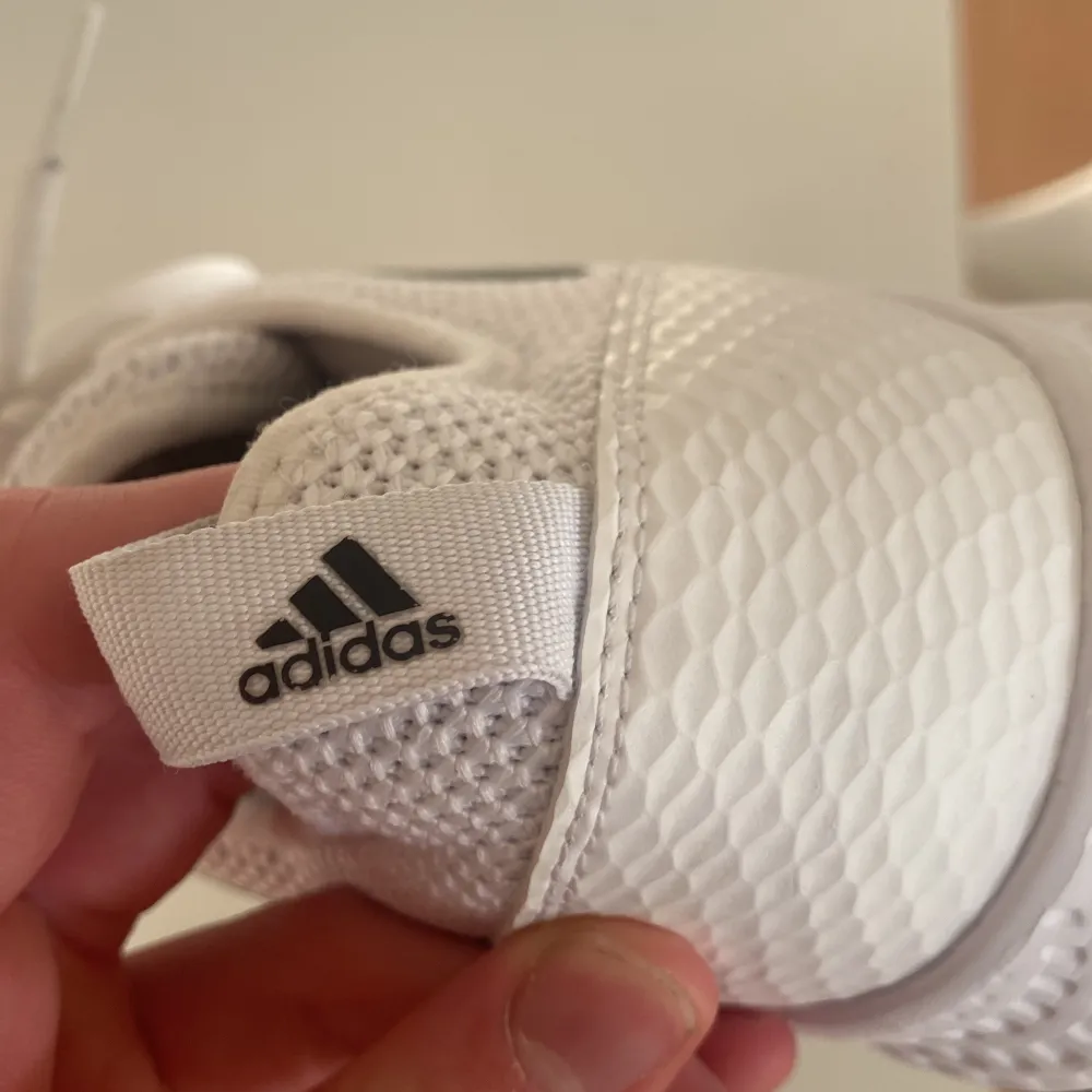 Säljer ett par vita Adidas sneakers i bra skick. De har en snygg design med svarta ränder och är gjorda av syntetmaterial. Perfekta för träning eller vardagsbruk. Det finns en liten skada på ena skon, men inget som påverkar användningen. Skorna har snörning och är märkta med 'End Plastic Waste'.. Skor.