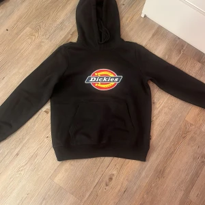 Svart hoodie från Dickies - Säljer en svart hoodie från Dickies i storlek S. Den har en stor logga på framsidan och en praktisk magficka. Perfekt för höst och vinter, och den är i mycket bra skick. Grym för både chill och vardag!