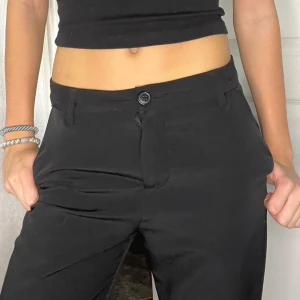 Svarta kostymbyxor från Lindex - Säljer ett par stilrena svarta kostymbyxor från Lindex i storlek 158. De har en klassisk design med knapp och dragkedja framtill. Perfekta för både vardag och festliga tillfällen. Byxorna är i mycket bra skick och passar till alla säsonger. De är lite högmidjade men enkla att sy om.