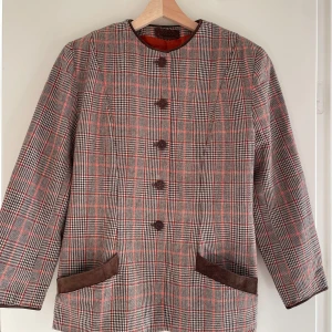 Rutig kavaj med bruna detaljer - Säljer en stilren rutig kavaj med bruna detaljer och knappar. Den har en klassisk passform och är perfekt för höst och vår. Kavajen har långa ärmar och är i mycket bra skick. Perfekt för en chic och tidlös look!