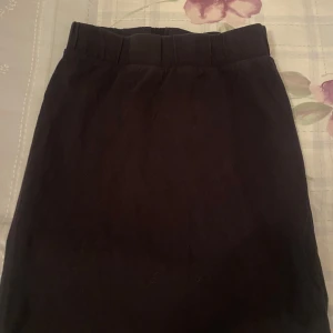 Svart kjol med bälte - Snygg svart kjol i mycket bra skick. Den har en stilren design med ett matchande bälte i midjan som ger en elegant touch. Perfekt för både vardag och festliga tillfällen. Kjolen är knälång och passar bra till olika toppar och skor.