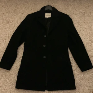 Svart rock från Bruun & Stengade - Snygg svart rock från Bruun & Stengade i storlek S. Den har en slim fit passform och är perfekt för både formella och semi-formella tillfällen. Rocken har långa ärmar och knappar framtill. Ett stilrent val för garderoben! Skicket är 9/10 (enbart använd förra vintern) och en väst som hör till rocken tillkommer. Bara att höra av sig vid frågor och pris går givetsvis att diskutera!