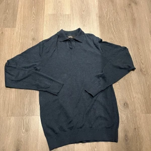 Mörkblå tröja från Dressmann - Säljer en stilren mörkblå tröja från Dressmann i storlek M. Tröjan är i bomull och har en klassisk krage med v-ringning. Perfekt för både vardag och lite finare tillfällen. Den är i mycket bra skick och bara använd två gånger