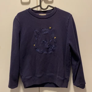 Mörkblå tröja från Maison Kitsuné - Säljer en snygg mörkblå tröja från Maison Kitsuné i mycket bra skick. Den har ett coolt kattmotiv med texten 'Maison Kitsuné' broderat på framsidan. Tröjan kostar originellt 1000kr men säljer för 750kr - pris kan diskuteras