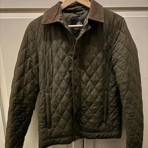 Olivgrön quiltad jacka från Henri Lloyd - Säljer en snygg olivgrön quiltad jacka från Henri Lloyd i storlek S. Jackan har en klassisk krage och knappar framtill. Perfekt för höst och vår med sin stilrena design Den är i mycket bra skick och redo för nya äventyr! 🍂