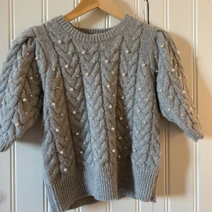 Grå stickad tröja med pärlor från Zara - Säljer en superfin grå stickad tröja från Zara. Den har ett snyggt flätmönster och är dekorerad med pärlor över hela tröjan. Perfekt för höst och vinter! Tröjan har trekvartsärmar och ribbade kanter. Passar både till vardags och festliga tillfällen. 💗💗