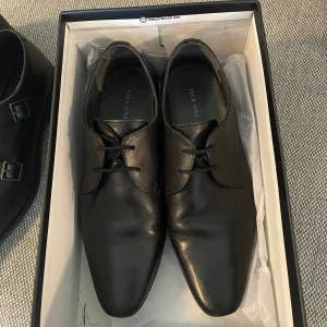 Svarta skinnskor med snörning - Snygga svarta finskor i mycket bra skick. Perfekta för formella tillfällen eller en stilren vardagslook. Skorna har klassisk snörning och en elegant design som passar till kostym eller jeans. De är bekväma och ger en sofistikerad touch till din outfit.