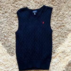 Mörkblå stickad väst, Ralph Lauren - Vi säljer en snygg mörkblå stickad väst från Ralph Lauren. Den har en klassisk V-ringning och det ikoniska röda logotypbroderiet på bröstet. Perfekt för lager-på-lager under höst och vår. Västen är i mycket bra skick och passar både till vardags och fest.