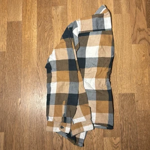 Rutig skjorta i jordnära toner - Säljer en snygg rutig skjorta i jordnära färger som beige, brun och grå. Skjortan har långa ärmar och knappar framtill. Perfekt för höst och vår, och funkar både till vardags och lite mer uppklädda tillfällen. Den är i bra skick och redo för en ny ägare!