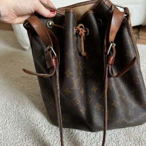 Louis Vuitton väska - Louis Vuitton (Noé) väska. Väskan är i bra skick för dens ålder. Eftersom modellen är från före 1980, så finns inget serienummer. Väskan är inköpt från Vestiaire Collective. Storlek 32 i höjd, 18 cm djup. 