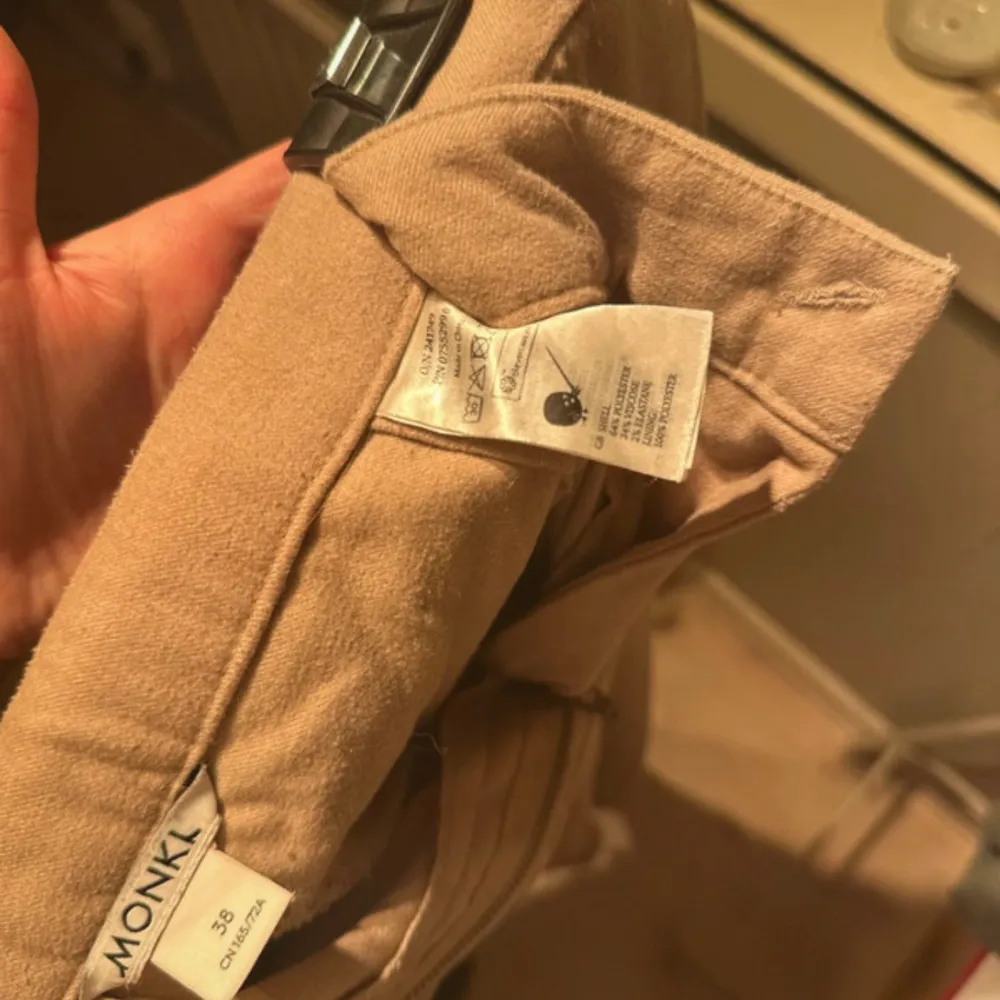 Säljer ett par snygga beige byxor från Monki i storlek 38. De har en stilren design med dragkedja och knapp framtill. Perfekta för både vardag och fest! 🕺. Farkut & Housut.