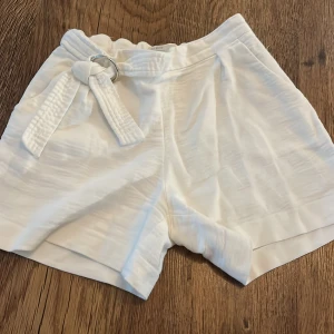 Vita shorts med knytband - Säljer ett par snygga vita shorts i mycket bra skick. De är högmidjade och har ett stilrent knytband i midjan som ger en fin detalj. Perfekta för sommardagar eller en avslappnad vårlook. Materialet känns lätt och bekvämt, vilket gör dem idealiska för både vardag och fest.