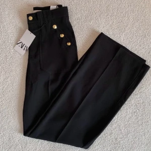 KOSTYMBYXOR MED GULDIGA KNAPPAR ZARA  - Svarta kostymbyxor med guldiga knappar frn ZARA. Högmidjad modell med rak utsvängd passform. Endast provat. I nyttskick, utan anmärkningar med tags kvar. Nypris 599