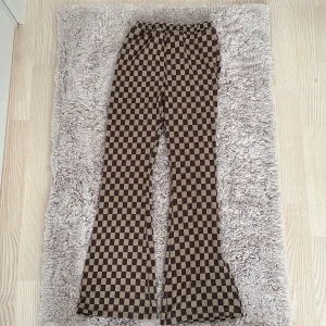 Brunrutiga byxor - Säljer ett par supercoola brunrutiga byxor i mycket bra skick. De har en skön och stretchig passform med hög midja och bootcut-stil. Perfekta för höst och vår, och de ger en retrovibe till vilken outfit som helst. Passar både till vardags och fest!. Har sytt den lite så att den skulle passa mig det går att ta bort storleken är 9-10 men skulle säga 7-8 