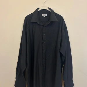 Svart skjorta från Smart Shirt Collection - Säljer en stilren svart skjorta från Smart Shirt Collection i storlek XXL. Skjortan har ett diskret mönster och är långärmad med knappar framtill. Perfekt för både formella och avslappnade tillfällen. Passar bra till höst och vintergarderoben.