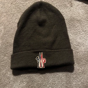 Mörkgrön stickad mössa från Moncler - Säljer en snygg mörkgrön stickad mössa från Moncler. Den har en broderad logga framtill i rött och vitt. Sparsamt använd och unik färg! Pris kan diskuteras🤩