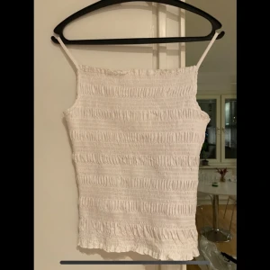 Vit ribbad topp - Säljer en söt vit ribbad topp med smala axelband. Toppen har en elastisk och bekväm passform. Toppen är i en strl L men är liten i strl så passar bättre på en M